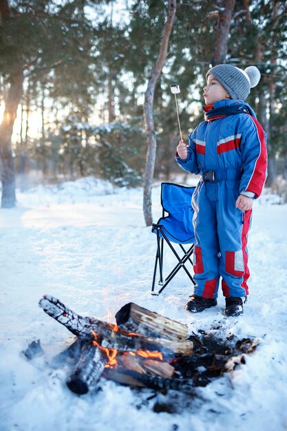 Familie winter picknick jongetje zit bij kampvuur in besneeuwd bos actief weekend