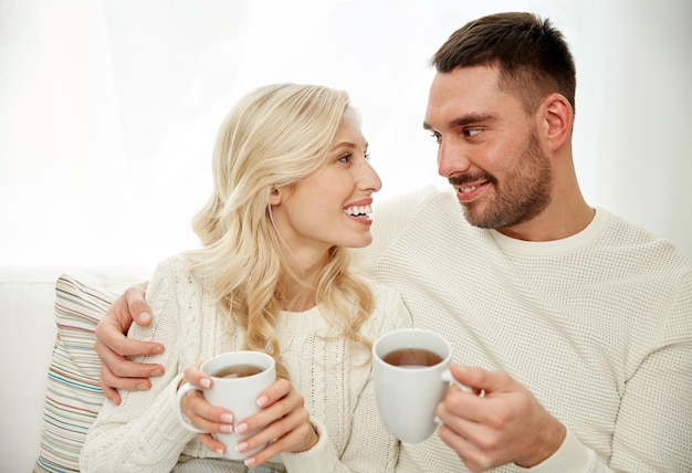 familie, winter, vakantie, liefde en mensenconcept - gelukkig paar met kopjes die thee drinken en thuis op de bank zitten