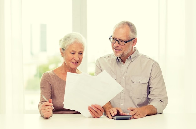 Familie, zaken, sparen, leeftijd en mensenconcept - glimlachend senior paar met papieren en rekenmachine thuis