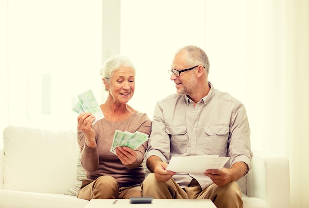 Foto familie, zaken, sparen, leeftijd en mensenconcept - glimlachend senior paar met papieren, geld en rekenmachine thuis