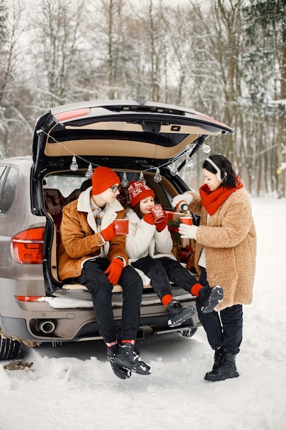 Familie zit in de kofferbak van een open auto in het winterpark en drinkt een kopje thee