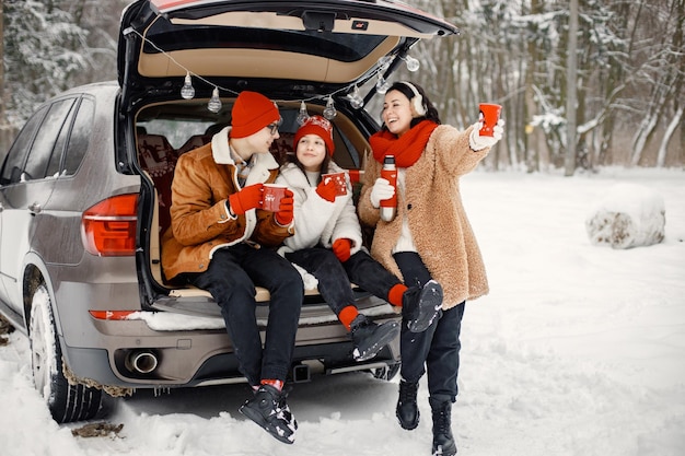 Familie zit in de kofferbak van een open auto in het winterpark en drinkt een kopje thee