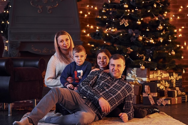 Familie zitten samen in kerst ingerichte kamer met nieuwjaarsboom.