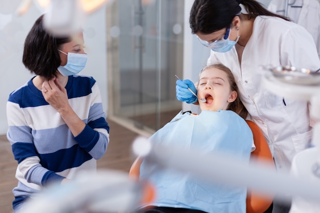 Familiebezoek bij tandartspraktijk voor tand- en mondhygiëne. Tandheelkundespecialist tijdens kinderholteoverleg in stomatologiekantoor met behulp van moderne technologie.