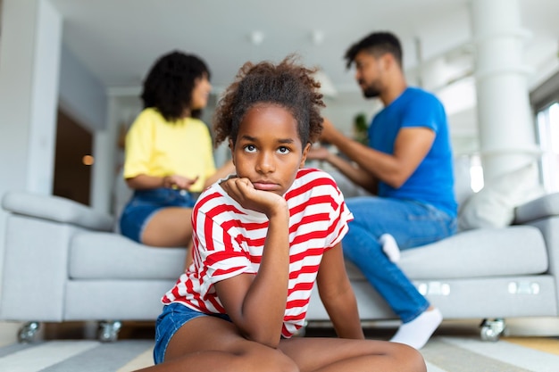 Familieconflicten Verdrietig klein zwart meisje dat wegkijkt terwijl haar ouders ruzie maken op de achtergrond boos kind wil geen ruzie horen gestrest kind dat alleen zit selectieve focus