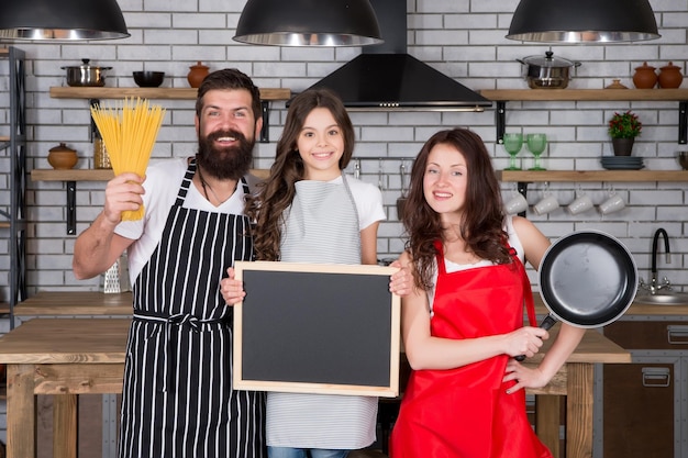 Familiedag Gelukkig gezin in de keuken Aangename tijd samen Recept voor een perfect familiediner Moeder en vader met een klein meisje dat de ruimte voor een schoolbord vasthoudt Meisje met ouders die koken