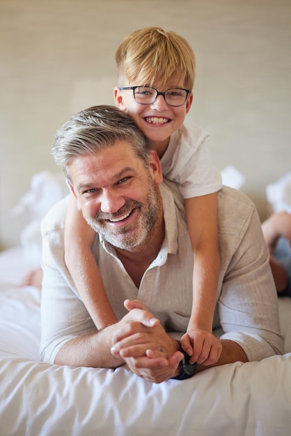 Familieliefde en kinderen met een vader en zoon die samen op bed liggen in een slaapkamer van hun huis Blij gezicht en glimlach met een portret van een man en zijn zoontje in hun huis om te ontspannen op een ochtend