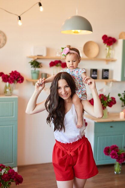 Familiemoeder en dochter met pioenenbloemen in keuken thuis. Gelukkig moeder en baby dochter. Gelukkig gezin.