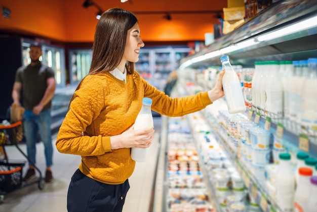 Familiepaar bij de vitrine met melk in de supermarkt, afdeling zuivelproducten