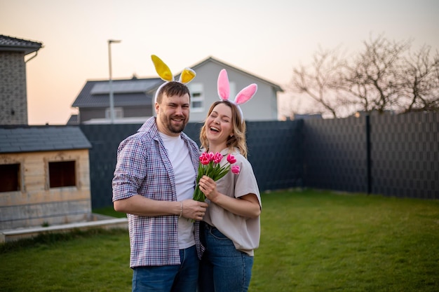 Familiepaar met konijnenoren die Pasen vieren man geeft zijn vrouw tulpen