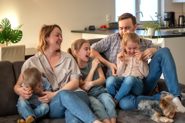 Familieportret familiefoto waarop moeder vader dochters zoon en hond lachend en knuffelend op de bank in een gezellige huiselijke sfeer