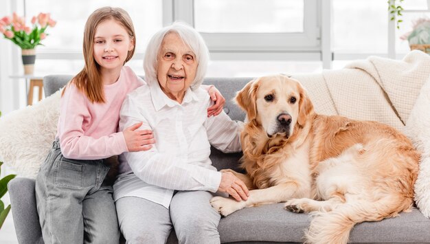 Familieportret van grootmoeder zittend op de bank met kleindochter en golden retriever-hond