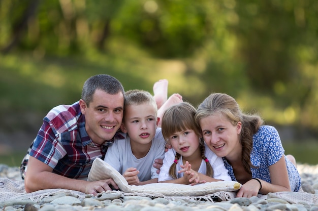 Familieportret van jonge gelukkige moeder, vader en twee schattige blonde kinderen, jongen en meisje op heldere zomerdag met groene bokeh. Gelukkig familierelaties, liefde, zorg en perfecte vakantie concept