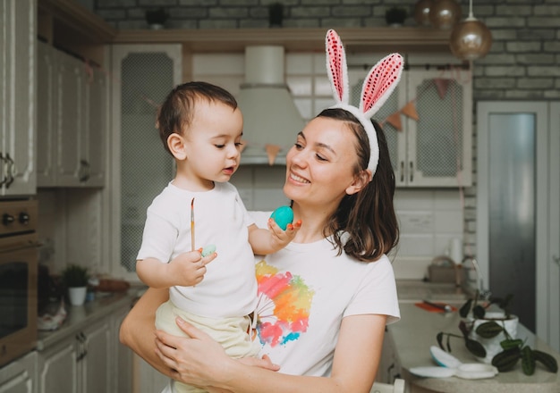 Familietradities voor Pasen Liefdevolle jonge moeder die kinderen leert hoe ze eieren moeten schilderen voor Pasen terwijl ze samen aan de keukentafel zitten
