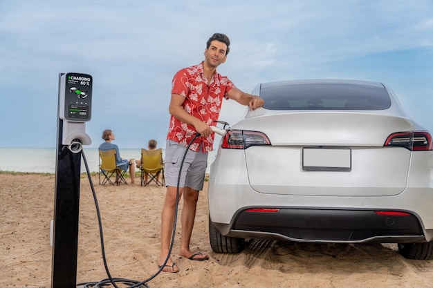 Familievakantiereis langs het strand met elektrische auto Papa of vader laadt EV-auto op terwijl zijn gezin geniet van het strand aan zee Familiereis met alternatieve energie en milieuvriendelijke auto Eeuwigdurend