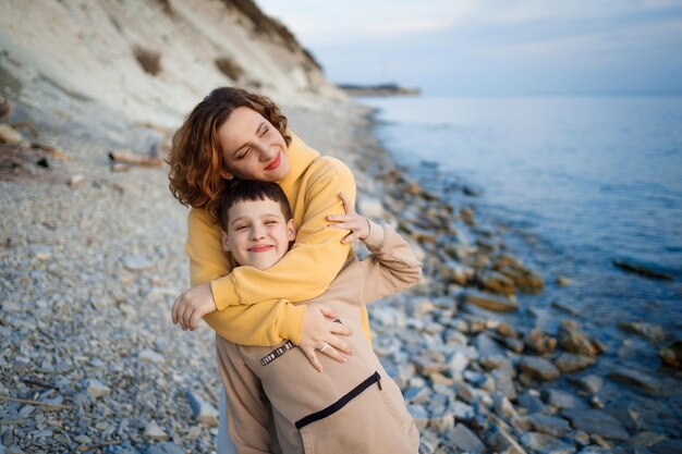 Familiewandeling aan de kust in het koude seizoen gelukkige moeder en zoon knuffelen elkaar