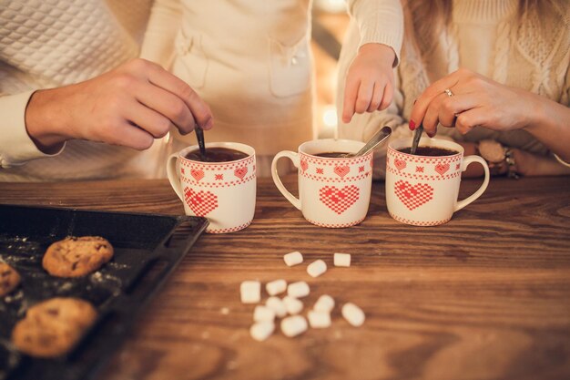 Familiewitte truien koken en drinken cacao met marshmallows Close-up handen en kopjes