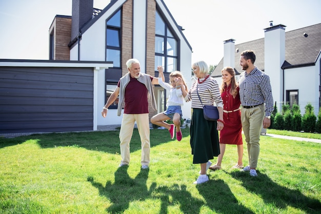 Family activities. Active grandpa looking at his granddaughter while walking together