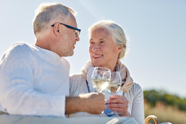 家族、年齢、休日、レジャー、人のコンセプト – 夏のビーチでピクニックをし、ワイングラスを鳴らす幸せな老夫婦