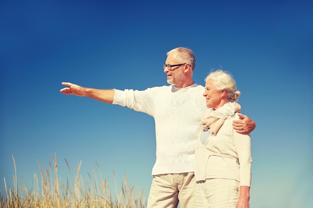 family, age, romance, leisure and people concept - happy senior couple pointing finger to something outdoors