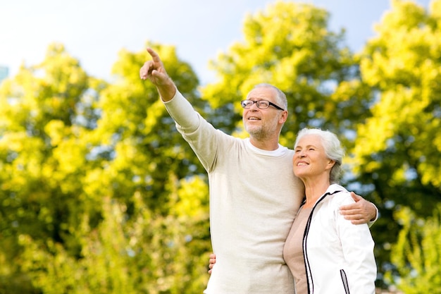 family, age, tourism, travel and people concept - senior couple hugging and pointing finger in park