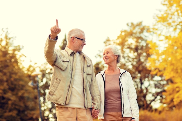 Concetto di famiglia, età, turismo, viaggi e persone - coppia senior che punta il dito e cammina nel parco