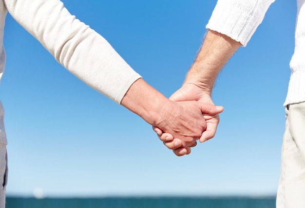 family, age, travel, tourism and people concept - close up of senior couple holding hands on summer beach