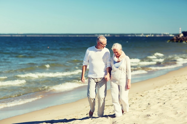 Photo family, age, travel, tourism and people concept - happy senior couple holding hands and walking on summer beach