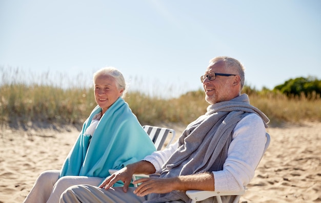 family, age, travel, tourism and people concept - happy senior couple resting in folding chairs on summer beach