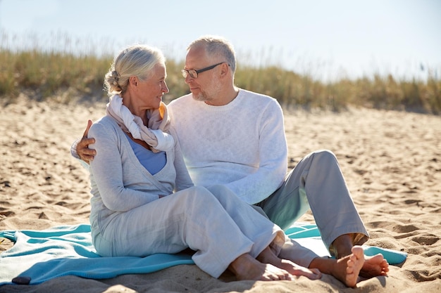 Photo family, age, travel, tourism and people concept - happy senior couple sitting on plaid and hugging on summer beach