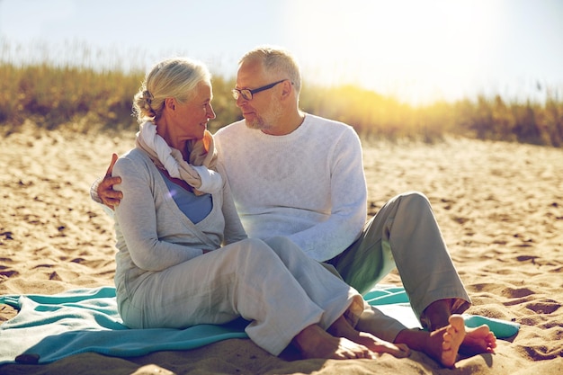 Photo family, age, travel, tourism and people concept - happy senior couple sitting on plaid and hugging on summer beach