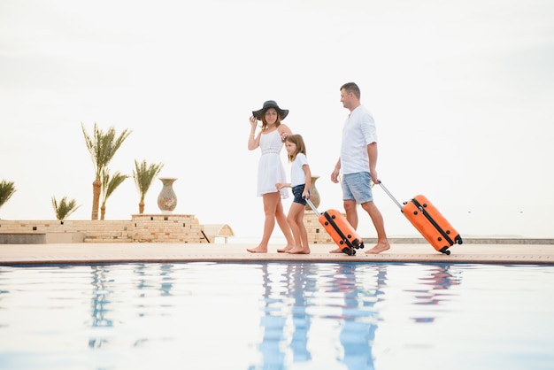 Family arriving to a luxury hotel with their suitcases by the swimming pool