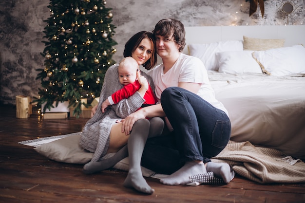 Family and baby sitting near Christmas tree at home