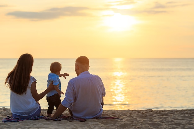 Family on the beach concept, Caucasian boy siting and holding sand on the tropical beach in sunset time 