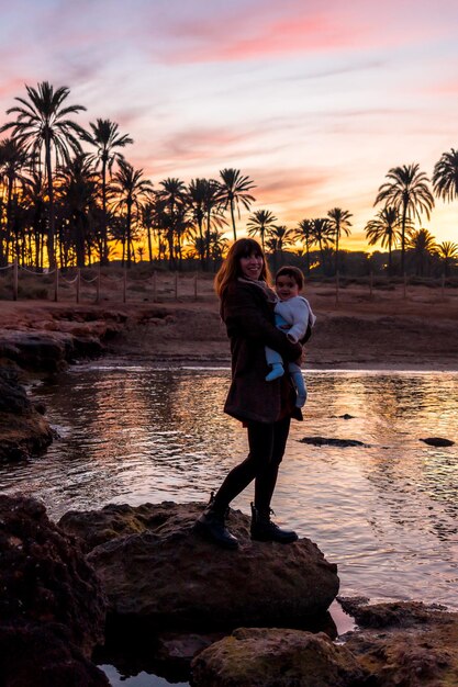 Famiglia sulla spiaggia giovane madre con il suo bambino in riva al mare al tramonto arancione