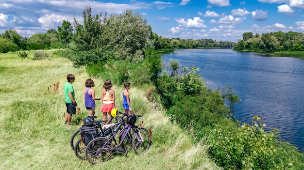 Famiglia in bici in bicicletta all'aperto, genitori e bambini in bicicletta, vista aerea aerea della famiglia felice con i bambini che si rilassano vicino al bellissimo fiume dall'alto, fine settimana e vacanze sport e concetto di fitness