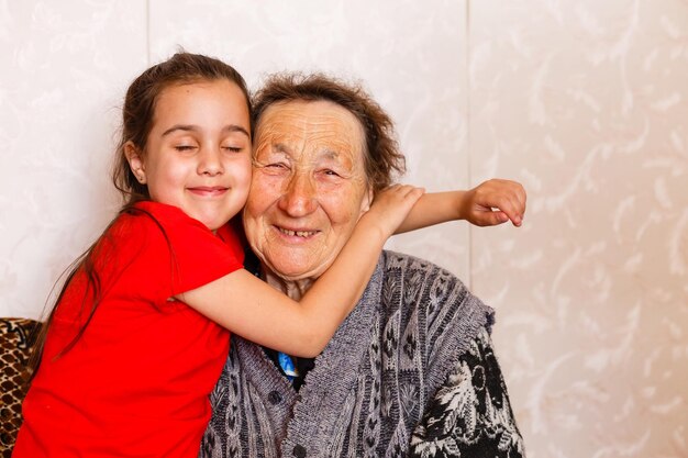 Family bonding concept. Lovely little girl happily emracing her grandma in light living room