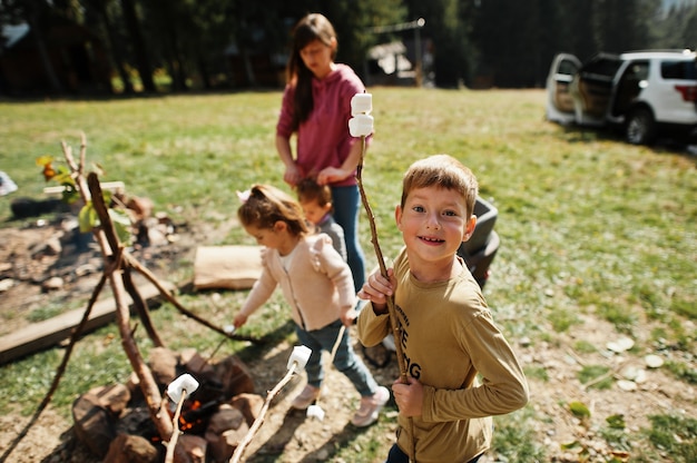 Family bonfire in mountain.four kids camping. bbq marshmallow.
autumn hike and camp weather. warming and cooking near flame
together.