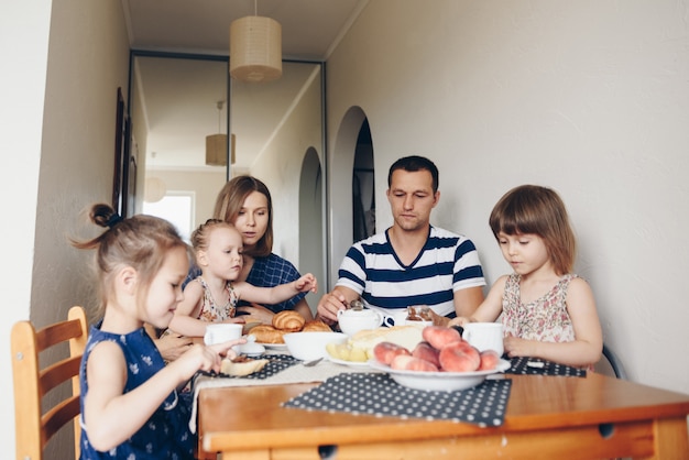 Family breakfast. Girls with parents sit at a table and eat croi