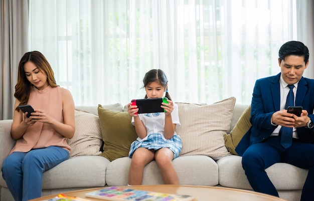 Family don't care about each other. Asian parents ignore their child and looking at their mobile phone at home, father and mother read social media but daughter play video game on sofa living room