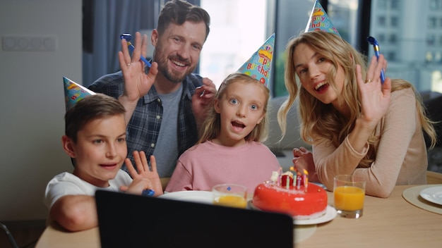 Family celebrating birthday online Mom dad kids waving hands laptop screen