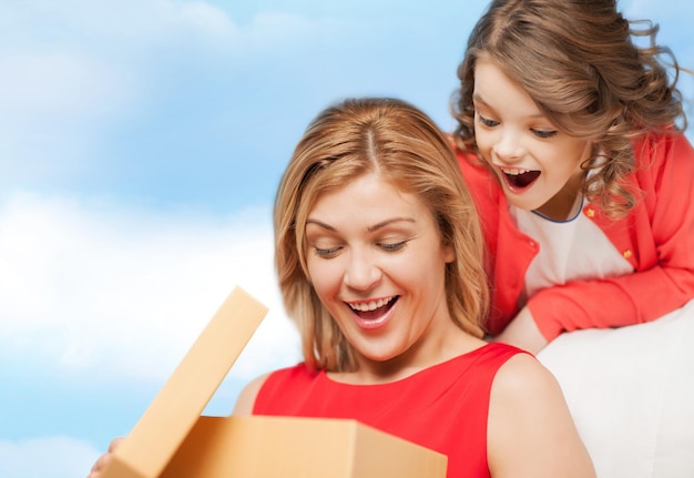 family, child, holiday and party concept - smiling mother and daughter with gift box