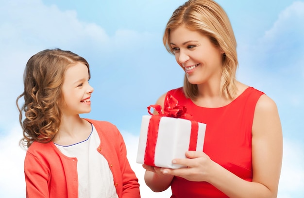 family, child, holiday and party concept - smiling mother and daughter with gift box