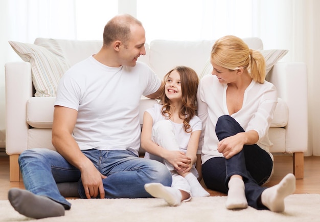 family, child and home concept - smiling parents and little girl sitting on floor at home