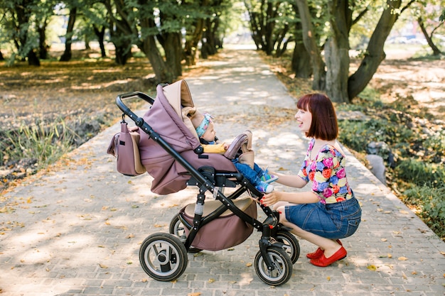 Семья, ребенок и концепция родительства - счастливая мать гуляет с коляской в парке со спины