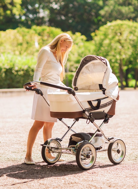 family, child and parenthood concept - happy mother with stroller in park