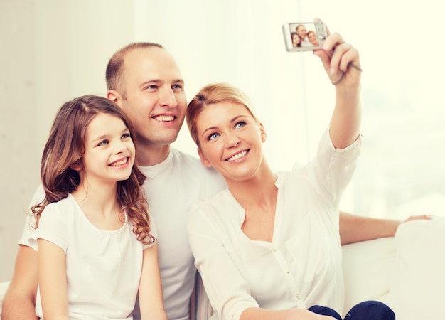 家族、子供、写真、家のコンセプト-デジタルカメラで自画像を作る小さな女の子と幸せな家族