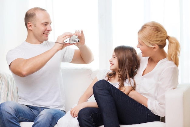 family, child, photography and home concept - smiling happy father taking picture of mother and daughter