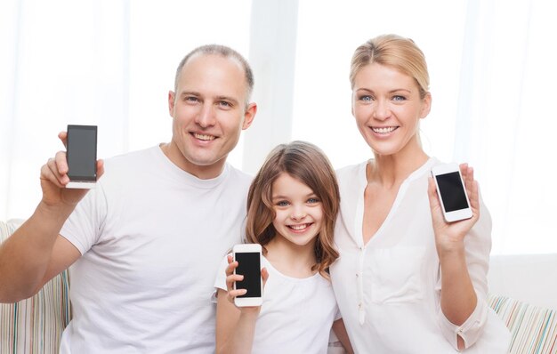 family, child, technology and home concept - smiling parents and little girl with blank black screen smartphones at home