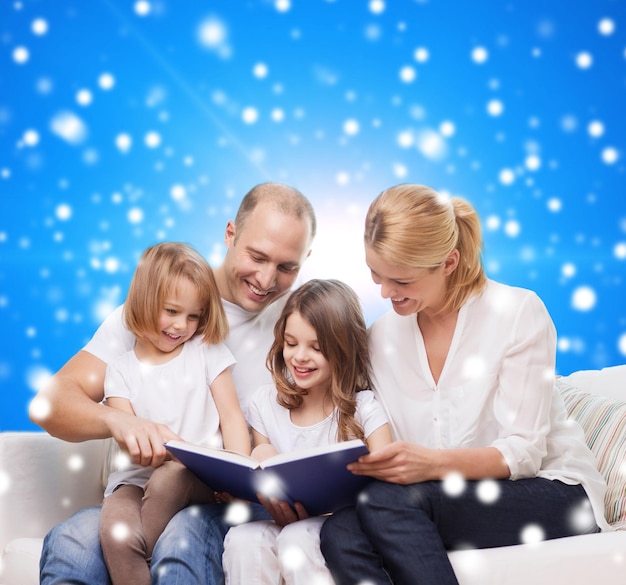 Фото Семья, детство, рождественские праздники и люди - улыбающиеся мама, папа и маленькие девочки читают книгу на голубом снежном фоне
